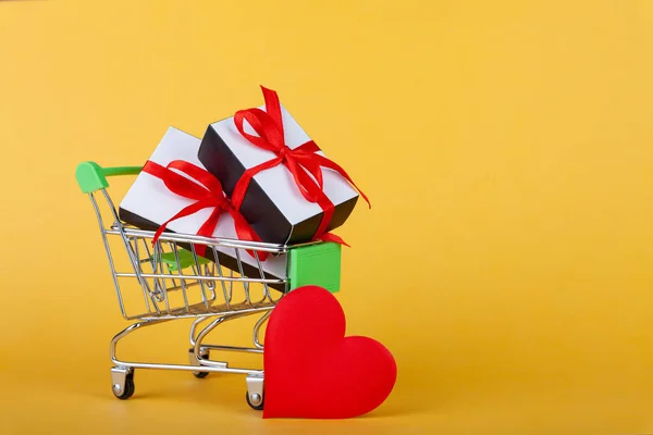 Corazón rojo, caja de regalo con cinta roja dentro de mini carrito de comestibles en fondo de color — Foto de Stock
