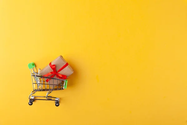 Caja de regalo con cinta roja en mini carrito de comestibles sobre fondo rosa — Foto de Stock