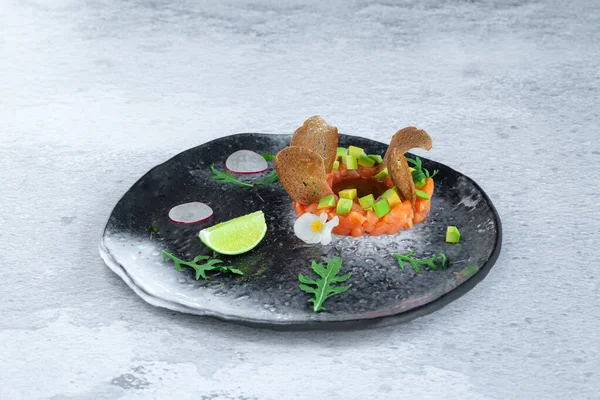 Portion of fresh salmon and avocado tartar on black plate — Stock Photo, Image