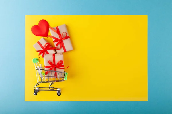 Corazón rojo, caja de regalo con cinta roja dentro de mini carrito de comestibles en fondo de color — Foto de Stock