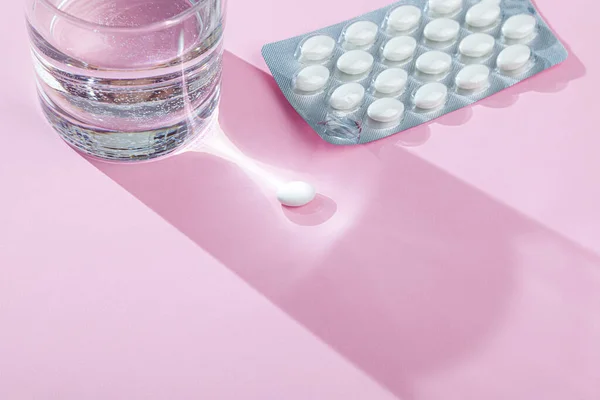 Bicchiere d'acqua, blister con pillole mediche, compresse, vitamine su sfondo rosa — Foto Stock