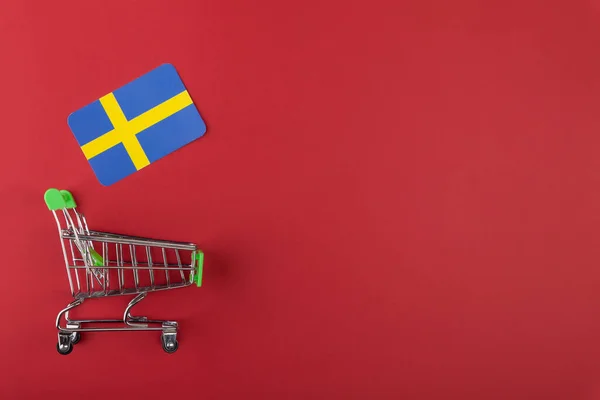 Mini carrito de la compra del supermercado vacío, bandera de Suecia sobre fondo rojo Fotos de stock libres de derechos