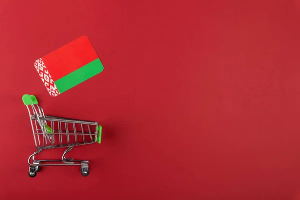 Mini carrito de la compra del supermercado vacío, bandera de Bielorrusia sobre fondo rojo Imagen De Stock