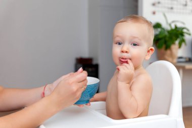 Annenin eli kaşıkla komik, mutlu, sarışın bir bebeği besler.