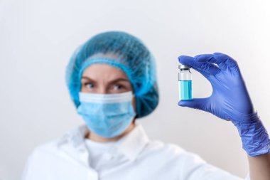 Eldivenli ve maskeli doktor şişeyi aşı ve ilaçla tutuyor.