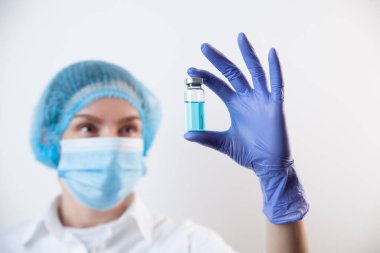 Eldivenli ve maskeli doktor şişeyi aşı ve ilaçla tutuyor.