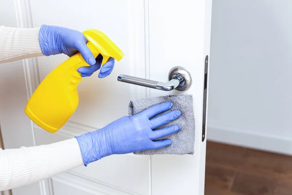 Manos en guantes desinfectando la manija de la puerta con trapo y detergente en aerosol Imágenes de stock libres de derechos