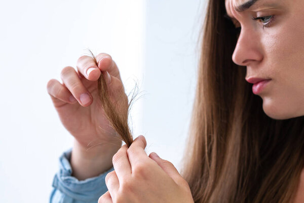 Portrait of upset unhappy sad woman with damaged lock of hair suffering from dry hair and split ends. Treatment and prevention hair problems