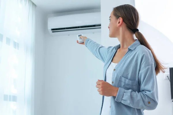 Young Woman Adjusts Temperature Air Conditioner Using Remote Control Room — Stock Photo, Image