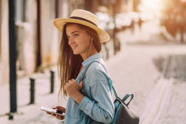 ヨーロッパの街の通りに沿ってバックパックやスマートフォンを歩くと帽子の女性を旅行 休暇と旅行生活 — ストック写真