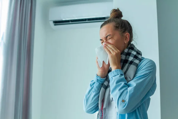 Sick sneezing woman caught a cold from the air conditioner at home