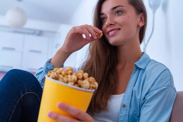 幸せな女性休んでいます上のソファと食べるカリカリポップコーンの間に映画を見ますホーム — ストック写真