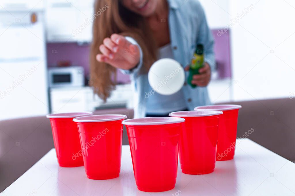 Woman with drinks having fun and enjoying beer pong game on table at home. 
