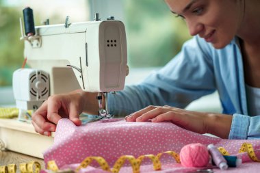 Dikiş makinesi kullanan terzi kadın ve dikiş dikmek için farklı aksesuarlar. 