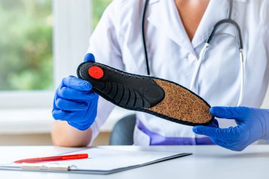Doktor düz taban tedavisi ve önlenmesi için ortopedik tabanlar tutuyor. Ayak bakımı