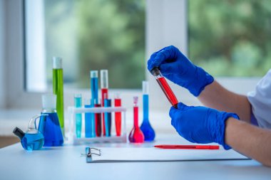 Laboratuvar asistanı klinik laboratuvar araştırması yapıyor. Elinde kırmızı sıvı test tüpü tutuyor. İlaç, eczane ve kozmetoloji kavramı. 