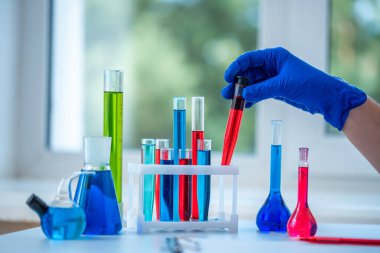 Laboratuvar asistanı klinik laboratuvar araştırması yapıyor. Elinde kırmızı sıvı test tüpü tutuyor. İlaç, eczane ve kozmetoloji kavramı. 