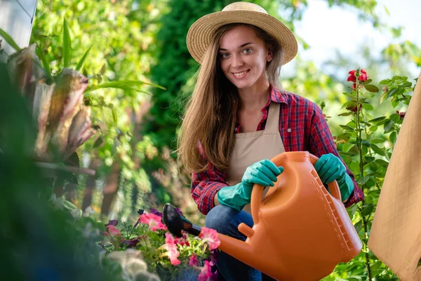 帽子とエプロンの幸せな笑顔の庭師の女性の肖像は 家庭の庭で散水缶で花を散水 園芸と花栽培 — ストック写真