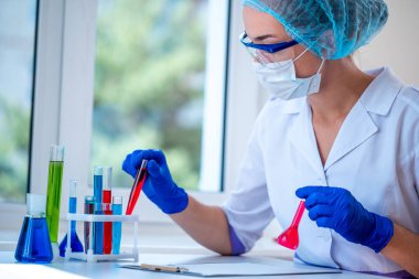 Kadın laboratuvar asistanı klinik laboratuvar araştırması yapıyor. Elinde renkli test tüpleri tutuyor. İlaç, eczane ve kozmetoloji konsepti. Test için bilimsel cam eşyalar. 