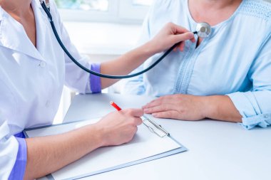 Genel tıp doktoru steteskoplu hastanın akciğerini ve kalp atışlarını dinler ve hastanede tıbbi muayene ve konsültasyon sırasında hastalığın teşhisini ve tedavisini yazar. 