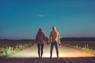 Tarlanın ortasında el ele tutuşup yıldızların düşüşünü izleyen aşıklar.