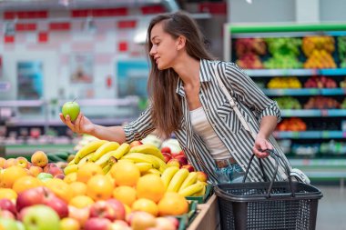 Kadın süpermarkette taze meyve seçiyor. Müşteri marketten yiyecek alıyor.