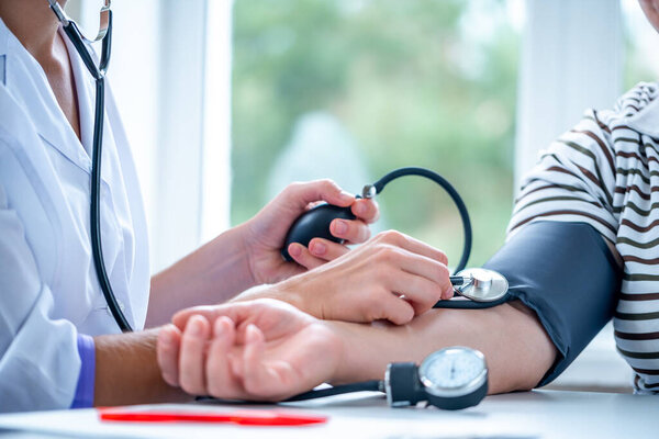 Врач измеряет кровяное давление пациенту во время медицинского осмотра и консультации в больнице. Здравоохранение 