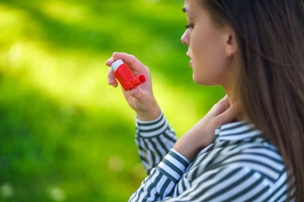 Asthmatic woman suffers from suffocation, allergic reaction and use inhaler from an asthma attack outdoor 