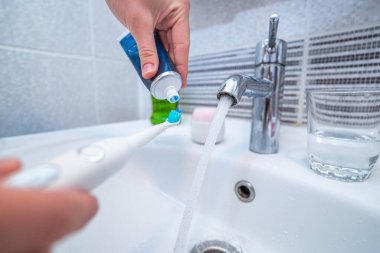 İnsan dişlerini ultrasonik diş fırçasıyla fırçalar ve diş fırçası olarak diş ürünleri kullanır ve evde banyoda temiz hava almak için. Ağız temizliği, diş ve diş sağlığı, sağlıklı dişler. Günlük yaşam ve rutinler 
