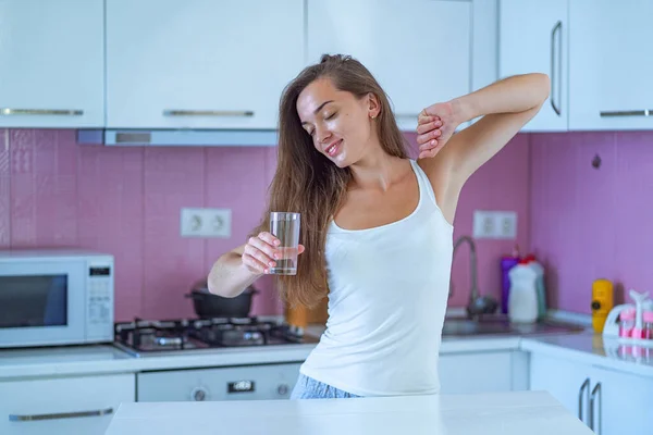 幸せな眠い女性がストレッチし 自宅で台所で目が覚めた後 早朝にきれいな精製された朝の水のガラスを飲みます 健康的なライフスタイル 新しい良い一日の始まりと始まり — ストック写真