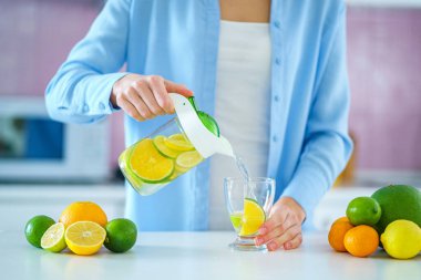 Woman pouring refreshing infused detoxification citrus water from jug in a glass for vitamin detox drink. Slimming antioxidant drinks for diet healthy drinking 