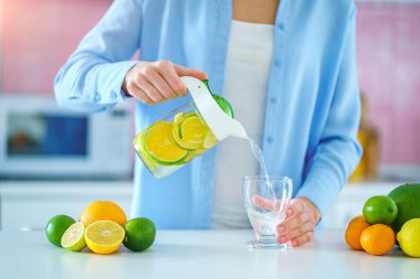Woman pouring refreshing infused detoxification citrus water from jug in a glass for vitamin detox drink. Slimming antioxidant drinks for diet healthy drinking 