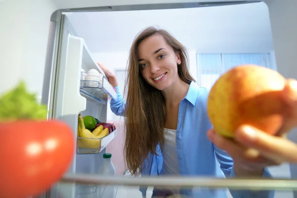 미소를 굶주린 여자가 냉장고에서 사과를 꺼내서 집에서 건강에 간식을 먹는다 — 스톡 사진