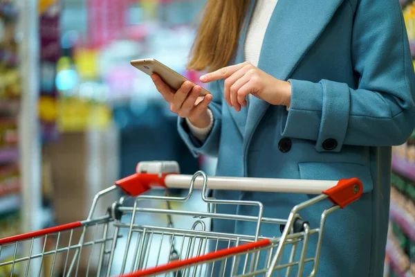 Mulher Comprador Com Carrinho Corredor Loja Com Lista Supermercado Smartphone — Fotografia de Stock