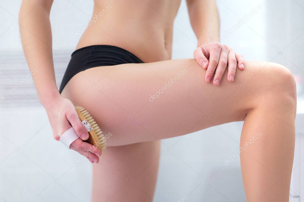 Woman brushing skin buttocks and butt with a dry wooden brush to prevent and treatment cellulite and body problem after shower in bathroom at home. Skin health