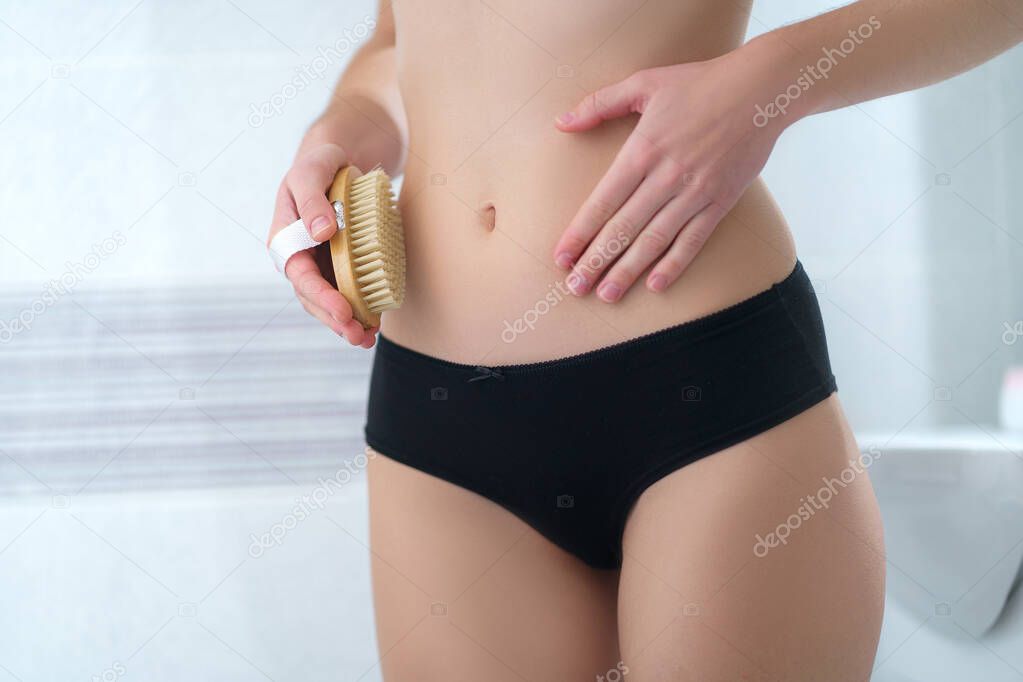 Woman brushing skin belly with a dry wooden brush to prevent and treatment cellulite skin and body problem. Skin health