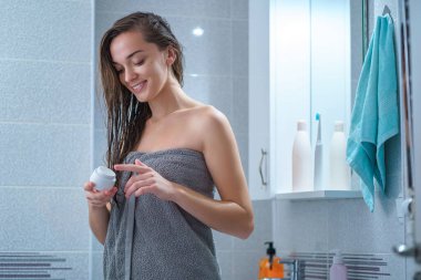 Banyodaki duştan sonra nemlendirici ve kuru deriyi nemlendirmek için banyo havlusu kullanan mutlu, beyaz, neşeli esmer kadın. Cilt kremi ve kadın bakımı 