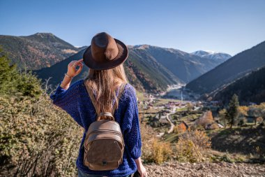 Stylish trendy free hipster woman traveler in a brown hat with backpack on a background of the mountains and uzungol lake in Trabzon during Turkey travel 