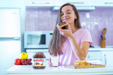 Batumi, Georgia - 11 Kasım 2019. Neşeli, yediği sandviçleri fındıklı çikolata ezmesiyle yiyen ve evde sabah kahvaltısında bir bardak taze süt içen mutlu bir kadın. 