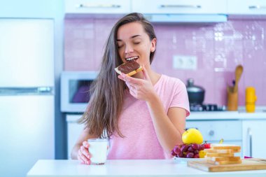 Happy joyful young breakfast woman eating toast bread with nut chocolate cream for a dessert at home 
