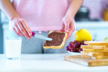 Woman spreads nut chocolate cream on toast bread for a dessert at home 