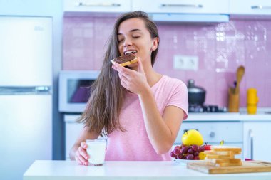 Happy joyful young breakfast woman eating sandwich with nut chocolate cream on a sweet healthy breakfast at home 