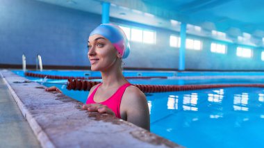 Spor yaparken mayo ve yüzme şapkası takan formda, atletik ve mutlu genç bir kadın yüzücü.