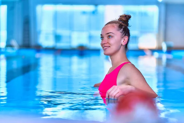 Young happy fitness swimmer woman in swimsuit enjoys relaxing in swimming pool in leisure centre, healthy lifestyle