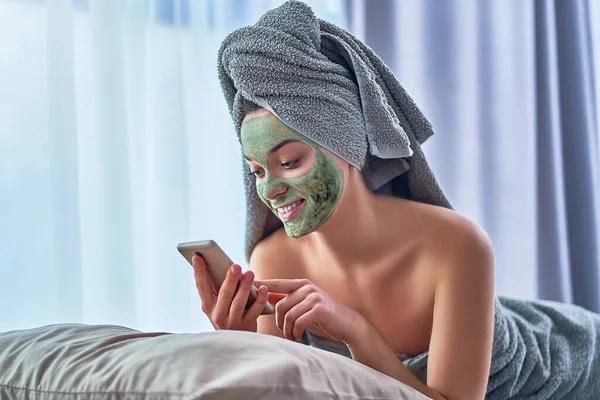 수건에 녹색의 마스크를 암컷이며 집에서 온천에서 샤워를 스마트폰을 사용하여 긴장을 — 스톡 사진
