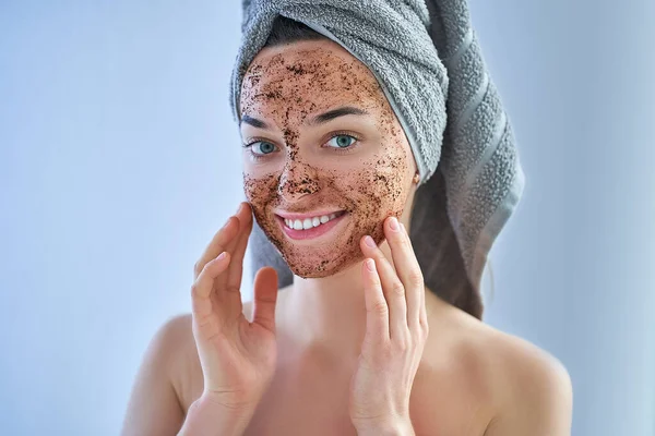 Portrait of smiling healthy happy woman in bath towel with natural face coffee scrub during spa day and skin care routine at home