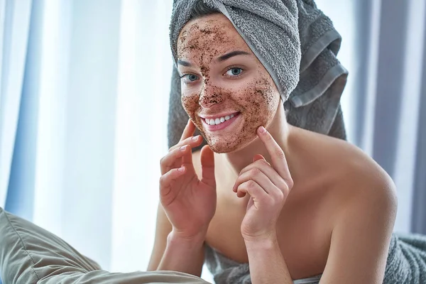 Portrait of smiling happy woman in bath towel with natural face coffee scrub mask after shower during spa day and skin care routine at home