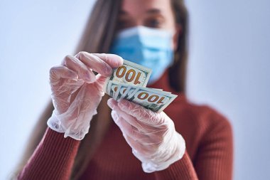 Tıbbi koruyucu maskeli ve koruyucu eldivenli kadın grip salgını ve koronavirüs salgını sırasında dolarları sayıyor. Virüs para konsepti. Virüslere, mikroplara ve bakterilere karşı koruma