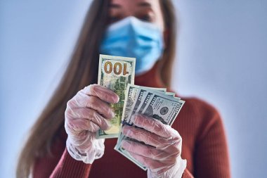 Tıbbi koruyucu maskeli ve şeffaf koruyucu eldivenli kadın para sayıyor. Grip salgını ve koronavirüs salgını sırasında sağlık ve el koruması. Virüs para kavramı