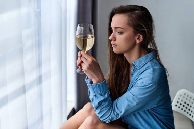 Depresyondaki üzgün, kederli, üzgün, gömlekli, kederli kadın şarap kadehi tutuyor ve depresyon ve endişeler sırasında evde tek başına oturuyor. Hayat sorunları  